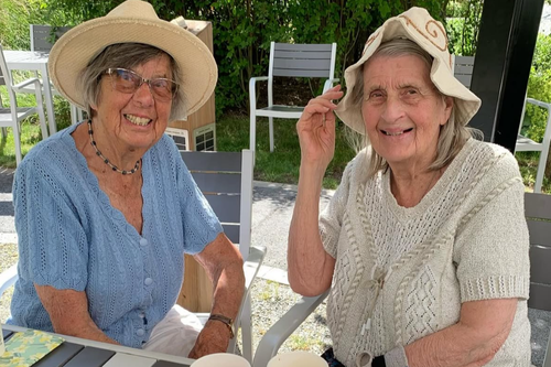 Tv&aring; boende sitter p&aring; uteplats i solhatt.