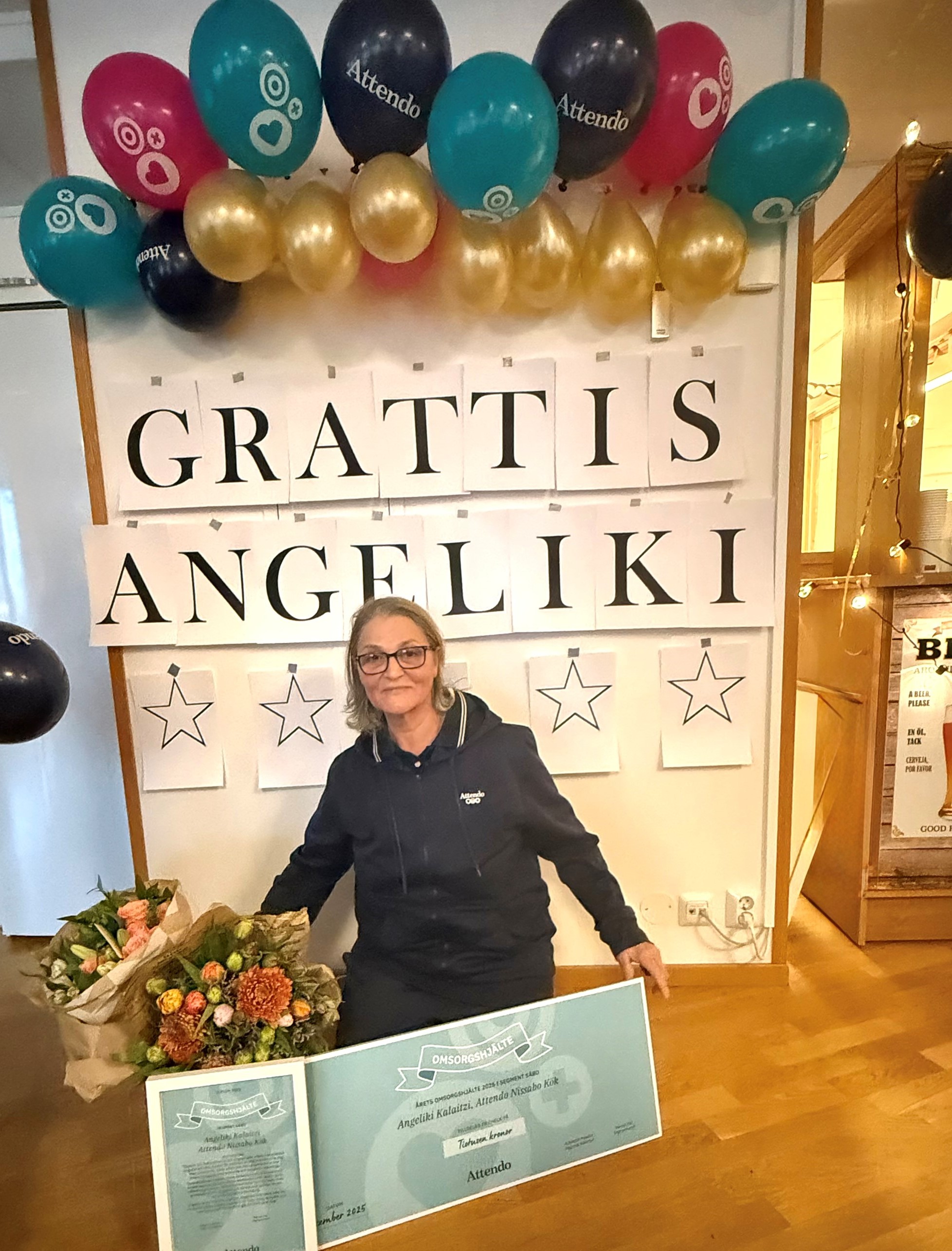 Angeliki sitter framf&ouml;r en stor grattisskylt, omringad av ballonger