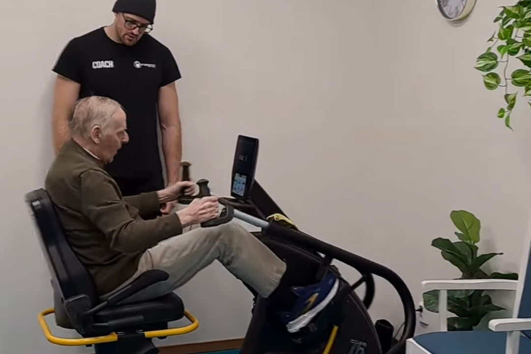 Man från äldreboendet tränar på en maskin och får coachning av tränaren