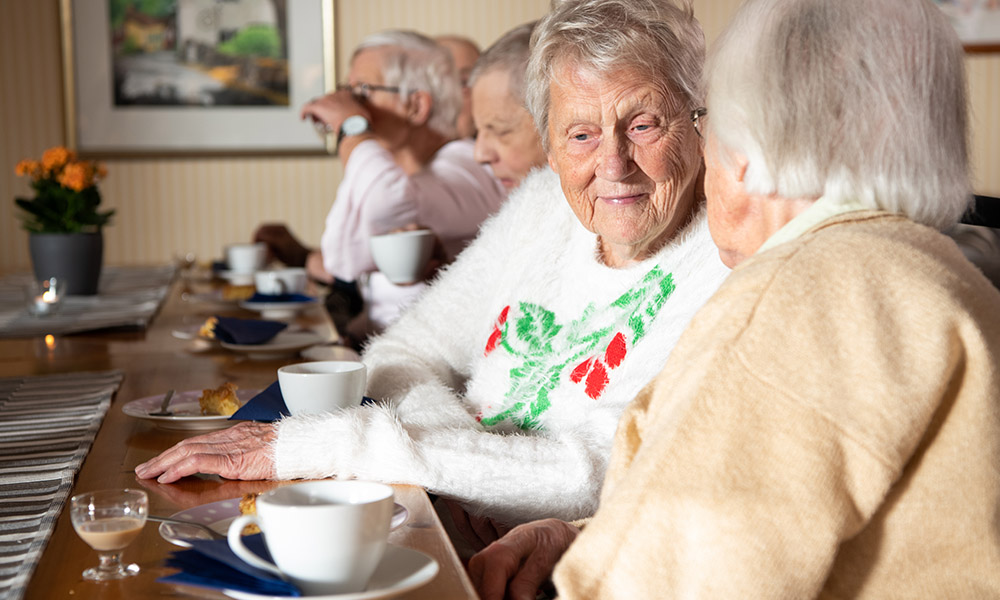 Äldre personer sitter vid ett bord och dricker kaffe i ett socialt samlingsrum