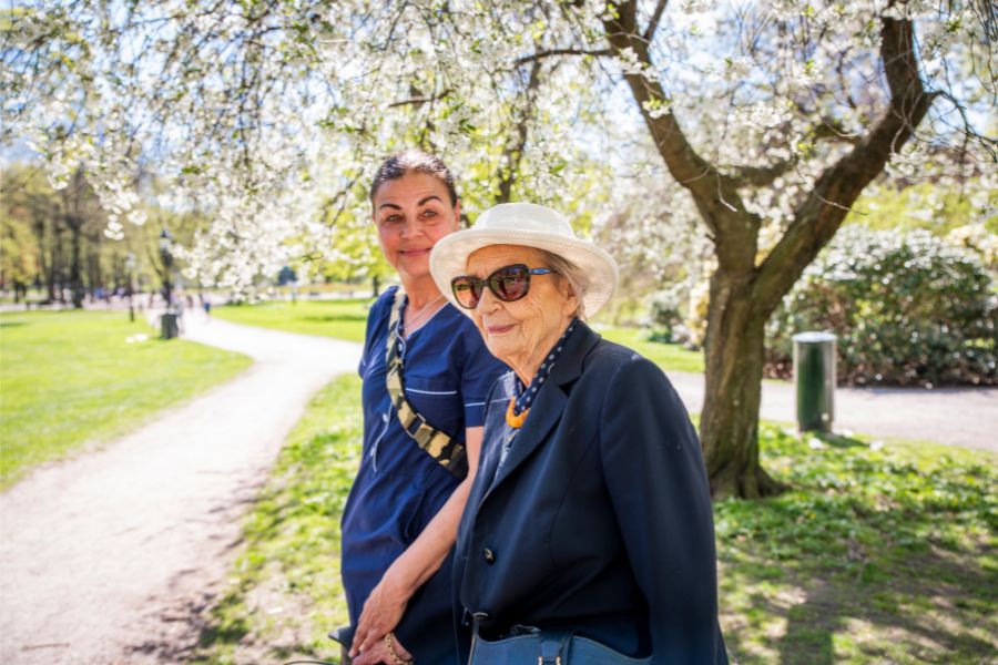 Äldre dam och hemtjänstpersonal promenerar tillsammans i park
